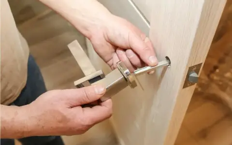 Hands assembling a modern door handle. A metal spindle is being inserted into the door mechanism, showing how to replace door handle.