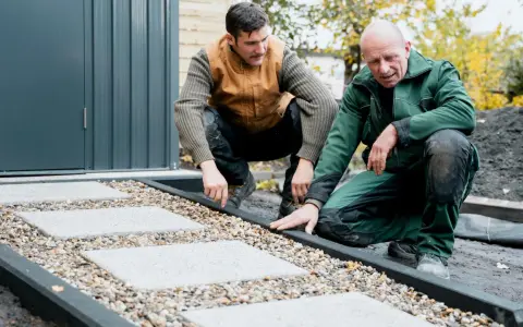 Zwei Männer arbeiten an einer neuen kies terrasse mit quadratischen Trittsteinen.