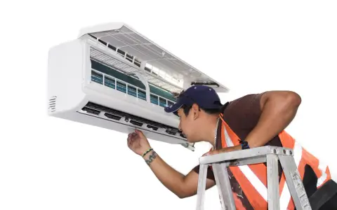 Un technicien vérifie un climatiseur mobile qui ne refroidit plus. Il est sur une échelle, examinant l'appareil.