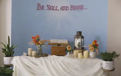 A serene scene for a midnight vigil: an open Bible, a lantern, and candles on a draped table, with "Be Still, and Know..." on the wall.