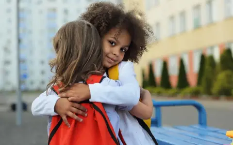 Zwei Kinder umarmen sich. Ein Mädchen mit Locken lächelt in die Kamera. Ein schönes Beispiel für Empathie bei Kindern.