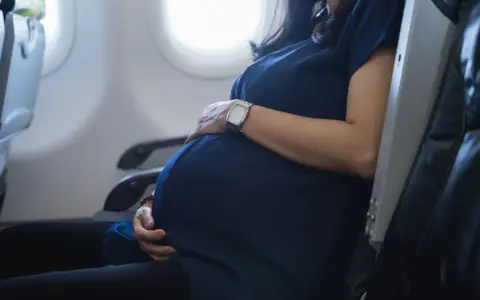 Eine schwangere Frau sitzt im Flugzeug und hält ihren Bauch. Sie fliegt entspannt in den Urlaub.