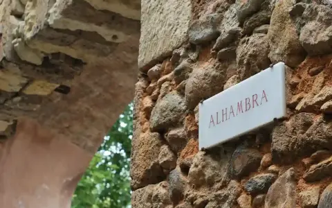 Schild "Alhambra" an einer alten Steinmauer, die zu einem Parkplatz führt.