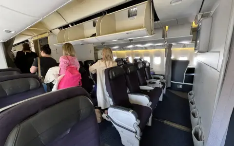 Wnętrze samolotu z rzędami foteli i pasażerami w przejściu.