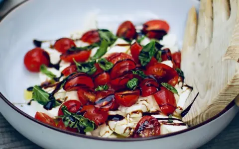 Frische Insalata Caprese mit saftigen Tomaten, cremigem Mozzarella und Basilikum, beträufelt mit Balsamico.