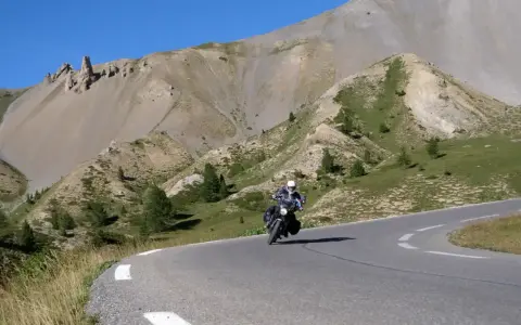 Motociclista percorre la route de grand alpes tra montagne scoscese e cielo azzurro.