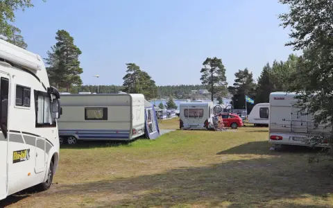 Solig dag på camping norrlandskusten med husbilar och husvagnar uppställda nära vattnet.