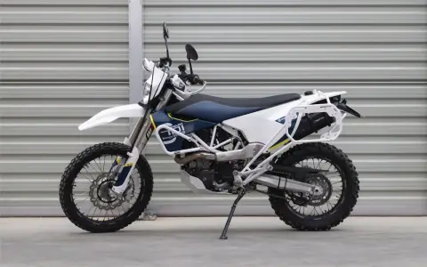 Biało-niebieski motocykl Husqvarna z bagażnikiem, gotowy na przygody w terenie. To idealny sprzęt do lekkiego enduro.