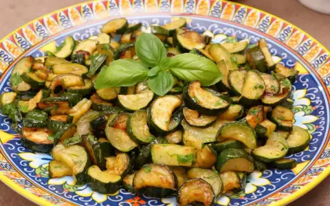 Zucchine trifolate dorate e saporite, guarnite con basilico fresco, servite su un piatto decorato.