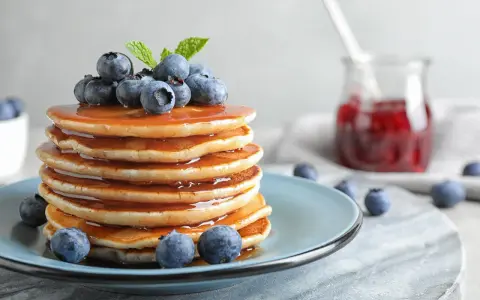 Stos puszystych pancakes polanych syropem, ozdobiony jagodami i miętą. Idealny przepis na pancake na śniadanie.