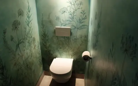Toilettes modernes dans une pièce aux murs recouverts d'un papier peint botanique bleu-vert. La **couleur toilette** est blanche, contrastant avec le décor.