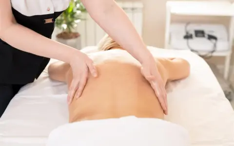 Relaksacyjny masaż kręgosłupa wykonany dłońmi terapeuty. Skóra lśni od olejku, a ruchy dłoni przynoszą ulgę.