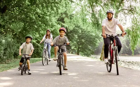 Familie genießt eine Fahrradtour mit Kindern in NRW. Vater, Mutter und zwei Jungen radeln auf einem asphaltierten Weg durch eine grüne Allee.