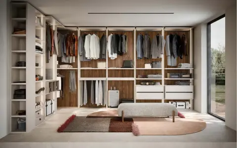 Ampia cabina armadio stanza con scaffali a vista, abiti appesi, cassettiere e un pouf centrale.