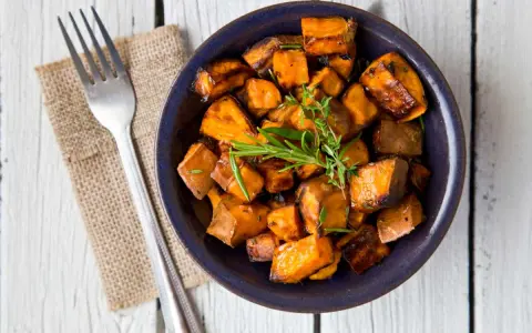 Patate douce air fryer croustillante, garnie d'herbes fraîches, servie dans un bol bleu avec une fourchette.