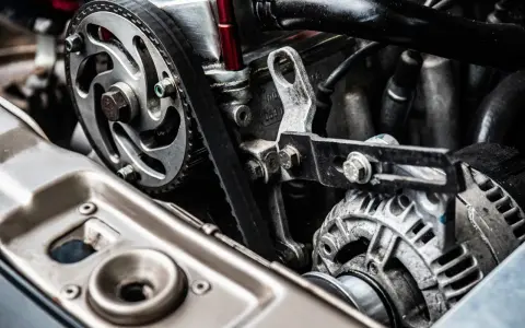Close-up of a car engine showing a toothed drive belt wrapped around a pulley and connected to an alternator.