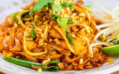 Un delicioso plato de pad thai con fideos de arroz, pollo, brotes de soja, cacahuetes picados y cilantro fresco.