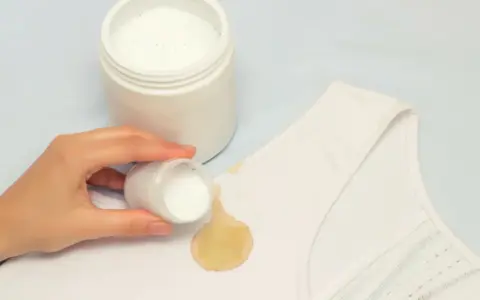 Mano aplica polvo blanqueador sobre mancha amarilla en ropa blanca. ¡Descubre cómo blanquear ropa blanca fácilmente!
