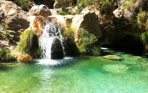 Cascada de agua cristalina cayendo en unas pozas turquesas, rodeadas de rocas y vegetación exuberante.