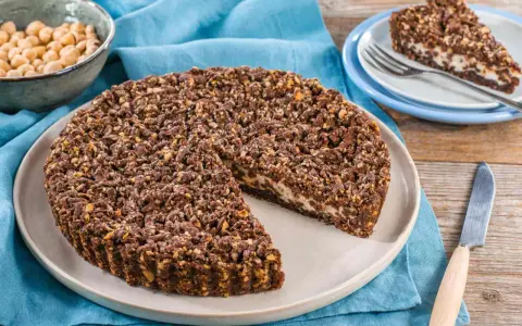 Sbriciolata ricotta e cioccolato con croccante copertura di nocciole. Una fetta invitante attende su un piattino.