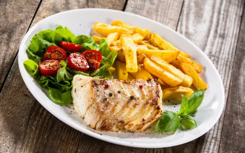 Idealne jakie przyprawy do ryby? Pieprz i sól na grillowanym filecie, obok frytki i sałatka z pomidorkami.