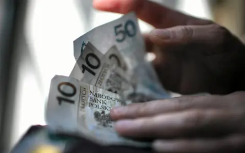 Dłoń trzyma polskie banknoty 10 i 50 zł. Zastanawiasz się, ile pieniędzy na bierzmowanie to odpowiednia kwota?