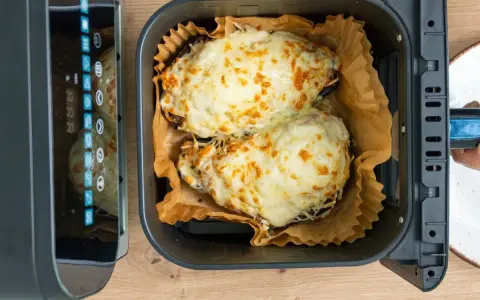 Dos mitades de berenjenas gratinadas con queso fundido, listas para disfrutar, recién salidas de la freidora de aire.
