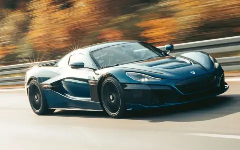 Blauer Rimac Nevera rast auf einer Straße, die Bäume im Hintergrund verschwimmen. Ein Beweis für die unglaubliche rimac nevera top speed.
