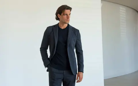 Uomo con giacca e pantaloni grigi, una mano nella tasca laterale del pantalone, mostrando i diversi tipi di tasche pantaloni uomo.