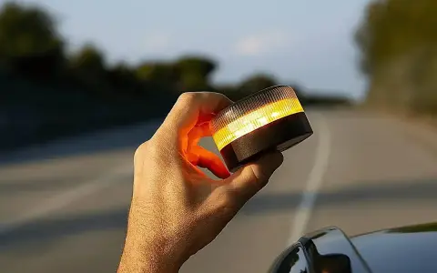 Mano sujeta una baliza de emergencia naranja brillante, lista para evitar una multa o señalizar un peligro en la carretera.