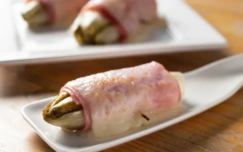 Endives au jambon sans béchamel, une recette simple et savoureuse. L'endive fondante enroulée de jambon sur une cuillère blanche.