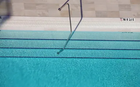 Escalera metálica en piscina de agua clara, con marcas de profundidad. El mantenimiento de piscinas es clave para su disfrute.