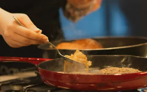 Cebolla caramelizada siendo removida con un tenedor en una sartén roja sobre el fuego.