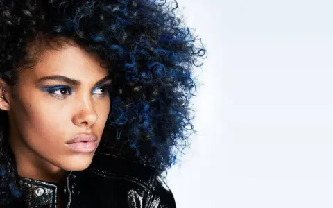 Mujer con cabello rizado negro azulado y maquillaje vibrante, luciendo una chaqueta brillante.