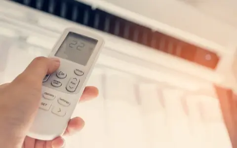 Mano ajustando el control remoto del aire acondicionado a 22 grados. ¿Cuántas frigorías por metro cuadrado necesita tu hogar para estar fresco?