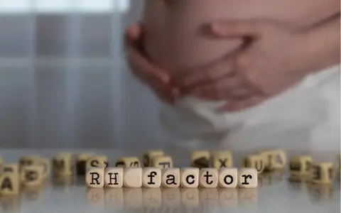 Ciąża i czynnik Rh. W tle brzuch kobiety, na pierwszym planie kostki z napisem "RH factor". Immunoglobulina w ciąży może być kluczowa.