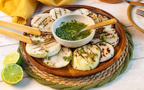 Gegrillte Kohlrabi-Scheiben mit Kräuter-Dressing und Limettenspalten auf einem Holzteller. Ein köstliches Gericht, das Lust auf Kohlrabi grillen macht.
