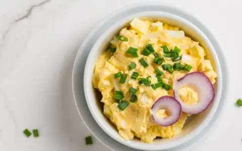 Pyszna pasta jajeczna z serem, posypana szczypiorkiem i ozdobiona krążkami czerwonej cebuli. Idealna na kanapki.