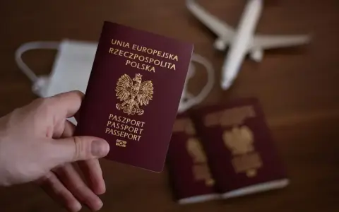 Dłoń trzyma polski paszport. Obok leżą kolejne dokumenty, maseczka i samolot. Zastanawiasz się, ile się czeka na paszport?