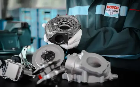 Mechanik w fartuchu Bosch Service prezentuje części turbosprężarki. Rozpoznaj uszkodzona turbina objawy i zgłoś się do serwisu.