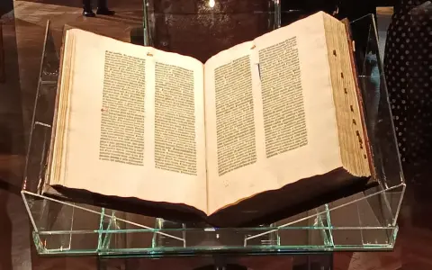 Otwarta biblia gutenberga pelplin, prezentowana na szklanym stojaku, świadectwo historii druku.