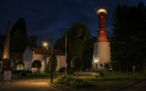 Nocna panorama latarni morskiej Rozewie z oświetloną wieżą i budynkami.