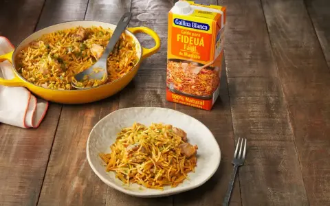 Un plato de fideos a la cazuela servido en una cazuela amarilla y en un plato blanco, junto a un cartón de caldo para fideuá.