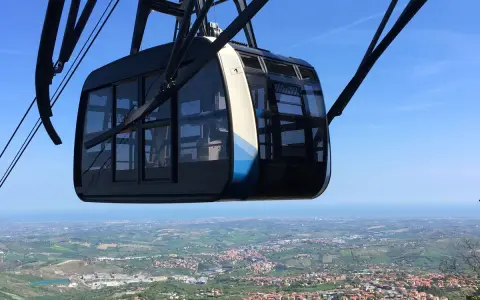 Cabina della funivia di San Marino in primo piano, con vista panoramica sulla città e sul mare all'orizzonte.