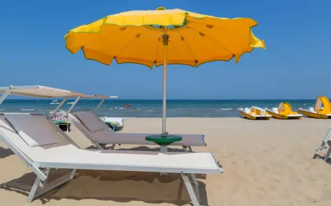 Spiaggia con lettini e ombrellone giallo, pedalò in attesa, mare calmo e cielo azzurro, tipico di tanti paesi vicino Rimini sul mare.
