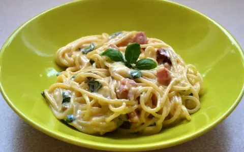 Spaghetti carbonara ze śmietaną, podane w zielonej misce, udekorowane bazylią. Pyszny przepis na klasyczne danie.