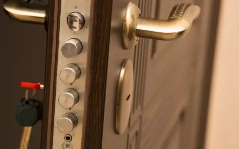 Poignée de porte blindée avec plusieurs serrures et une clé rouge. Des marques sur le cylindre supérieur suggèrent une tentative d'effraction.