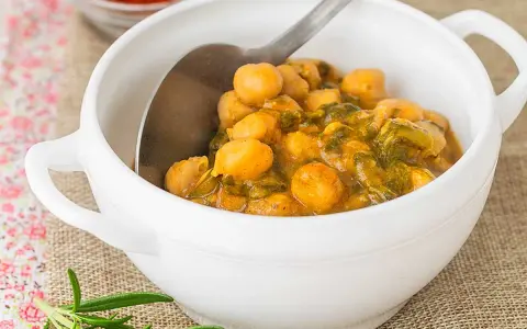 Un tazón blanco lleno de garbanzos con acelgas, un plato reconfortante y nutritivo.