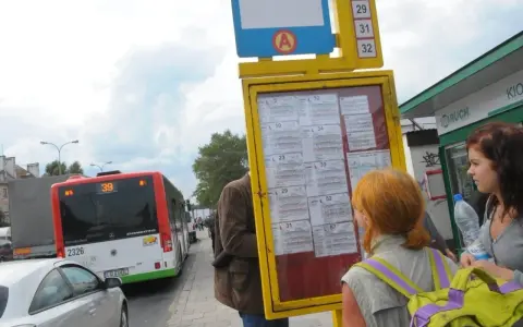 Ludzie sprawdzają 79 rozkład jazdy na przystanku. Autobus linii 39 stoi obok.