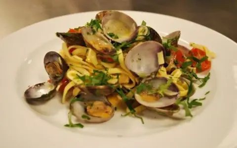 En tallrik med pasta vongole, där färska vongole-musslor blandas med tagliatelle, körsbärstomater och persilja.